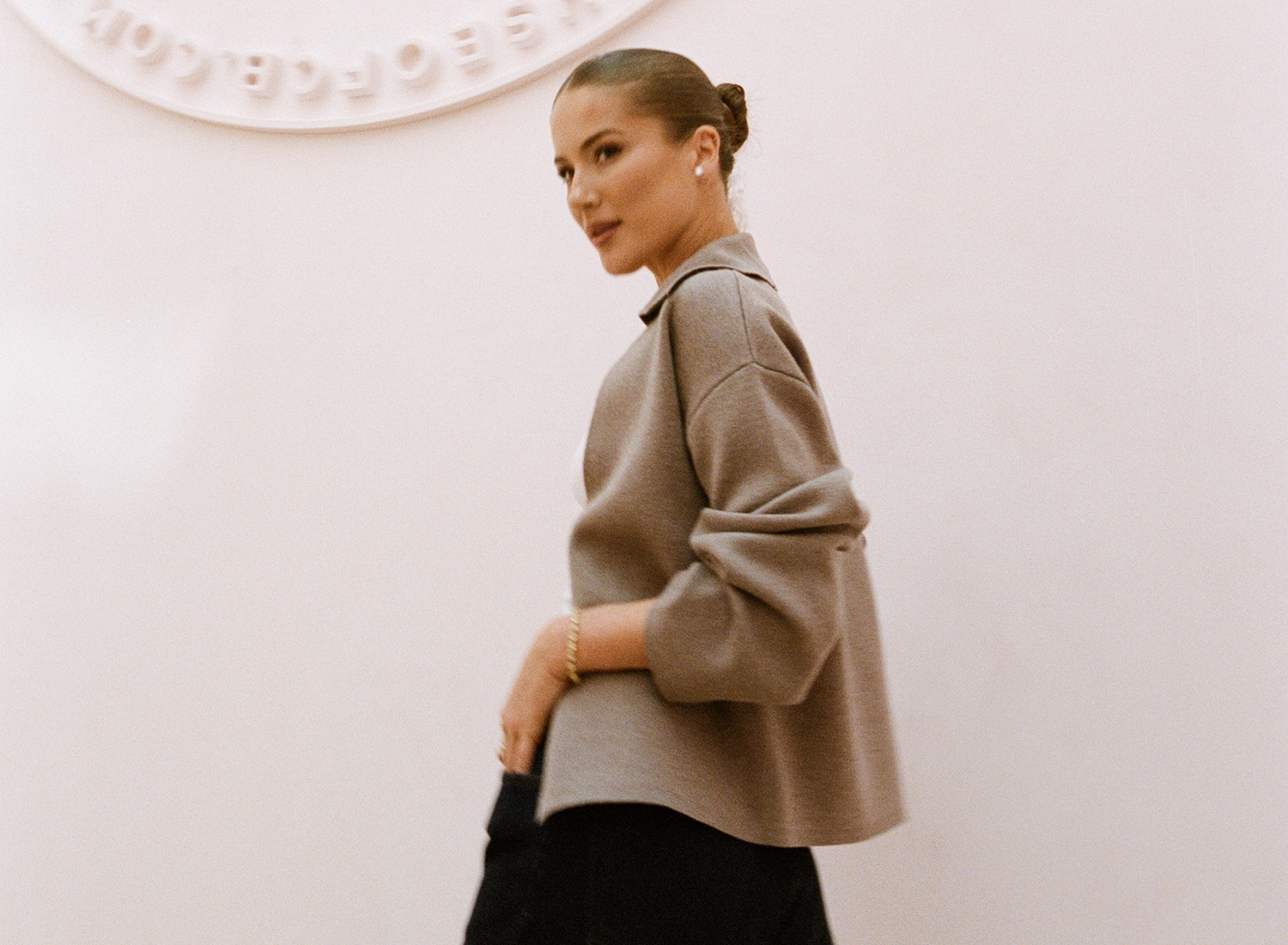 Conna Walker, House of CB founder, in a taupe collared knit jacket against the embossed wall seal